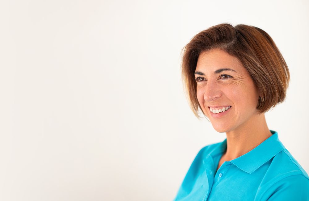 A woman, owner of her own physiotherapy clinic, smiles confidently, on a plain white background