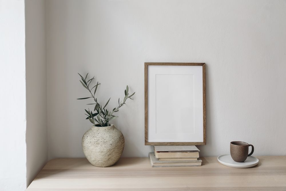 Wooden table with vase of eucalyptus branches, books and mug with mockup frame
