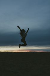 Silhouette of a woman jumping in a field with her arms up and knees bent