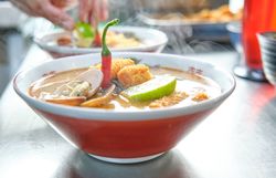 Hot soup with shellfish and noodles with topping in kitchen
