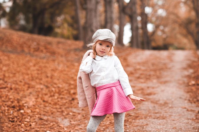 Young girl posing in pink skit and gray hat holding a jacket