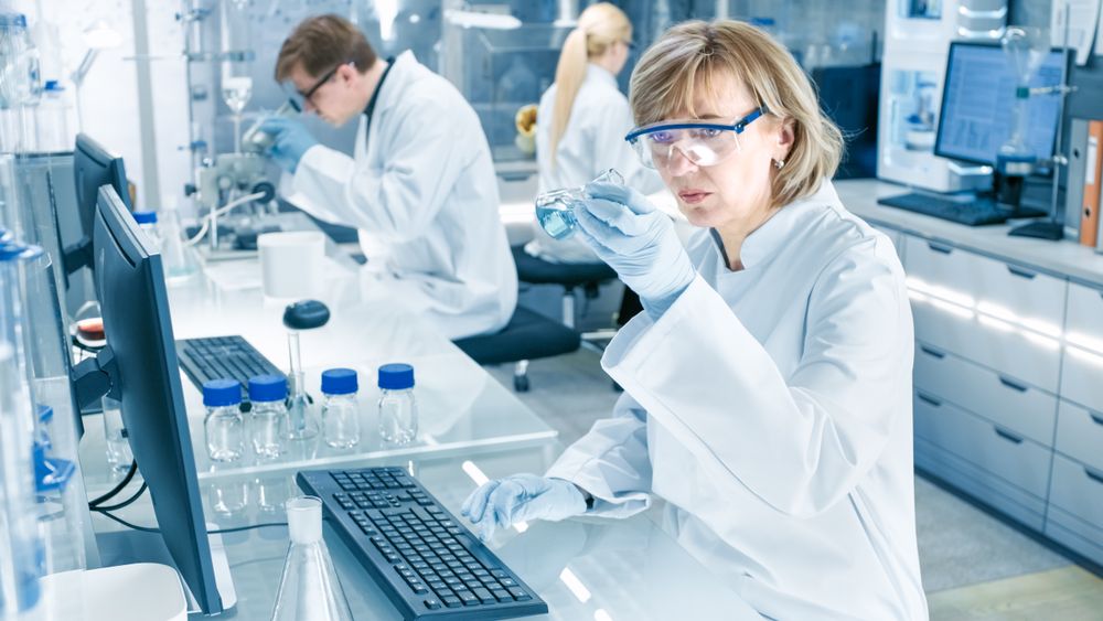 Female Scientist Analyzes Liquid in the Beaker and Types Down Observations on Her Computer.