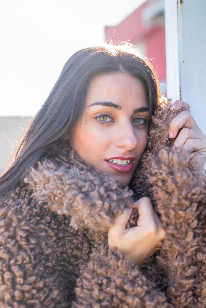 Cheerful woman wrapping in coat on street