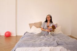 Woman in striped pajamas sitting on bed with stuffed toys.