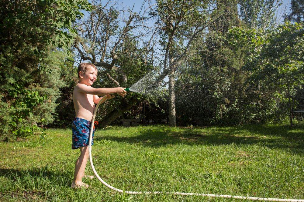 Little child having fun with garden hose and water