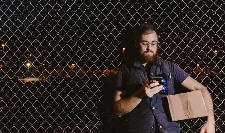 Courier with carton waiting client on street in evening