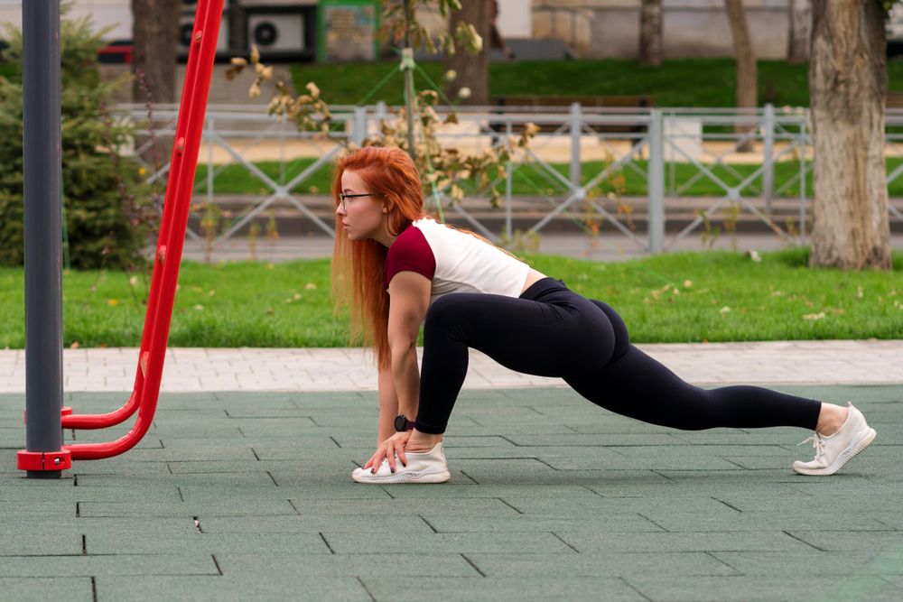 Woman in deep lunge stretch on outdoor fitness equipment