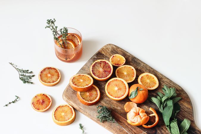 Whole and sliced tangerines and blood oranges fruits with thyme, mint herbs on wooden chopping board