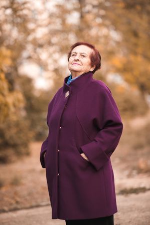 Older woman in purple coat standing near autumn trees