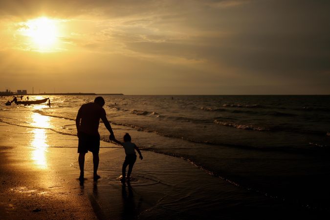 Back view of father and young daughter walking on beach during sunset