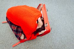 Woman trying to get into suitcase on road