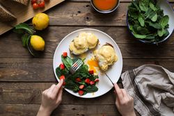 Person eating scrambled eggs on bread with green sauce and tomato