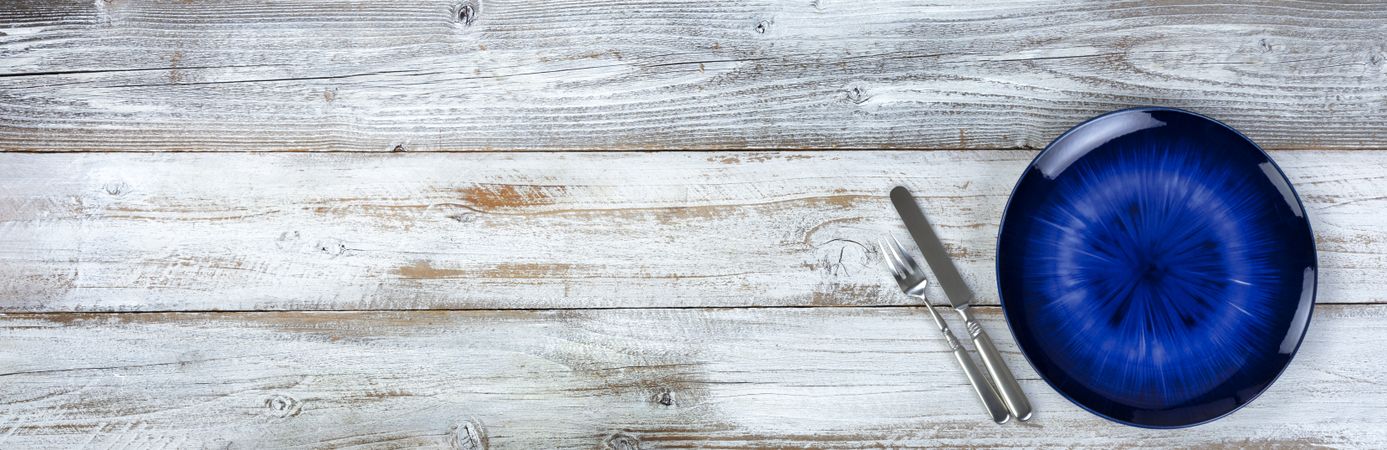 Basic table setting of an empty main dark blue dish with cutlery on wood