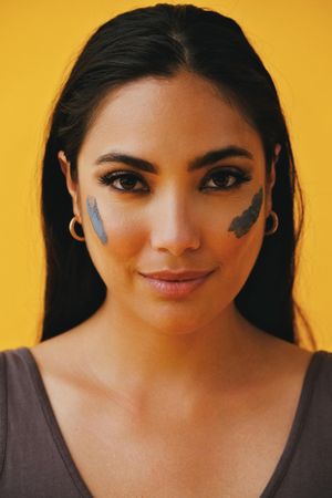 Smiling Latina woman standing with mud mask on face, vertical