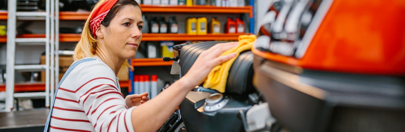 Mechanic woman cleaning motorcycle seat with cloth on factory
