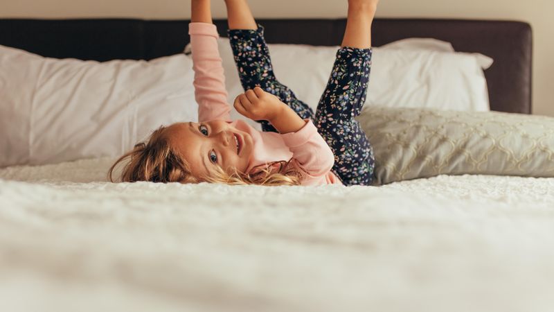 Little girl lying on bed playing with hands and legs raised