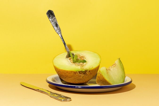 Sliced small melon on plate with spoon and fork