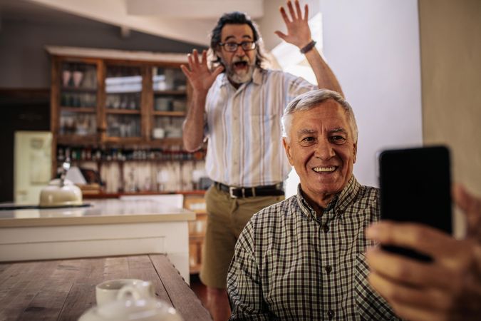 Happy man taking selfie with friend standing at back with his hands raised