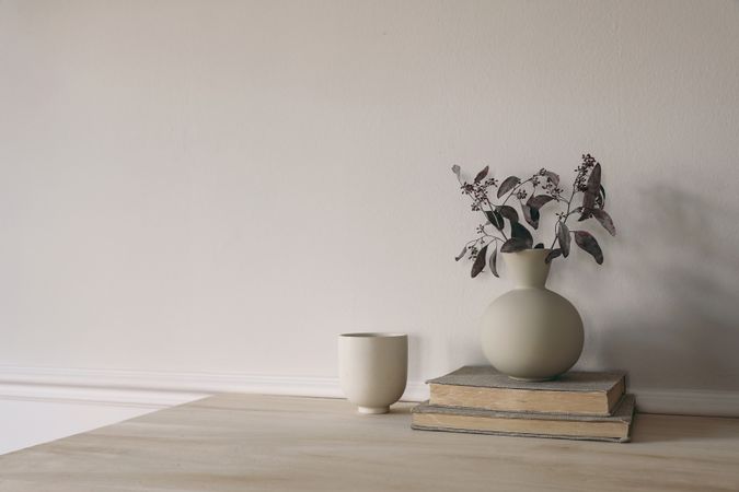 Modern vase with dry eucalyptus tree branches on wooden table. Cup of coffee, pile of old books.