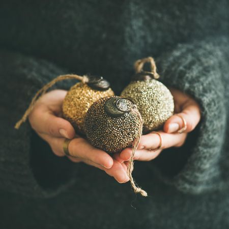 Woman with three gold Christmas tree decoration with her hands, square crop