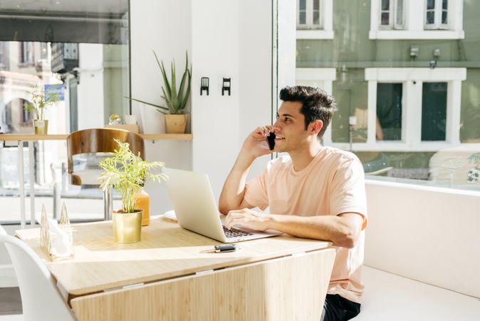 Crop man using laptop and talking phone in cafe
