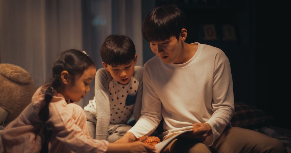 Korean Father Reading a Fairytale to His Lovely Cute Kids in Bed Before Going to Sleep.