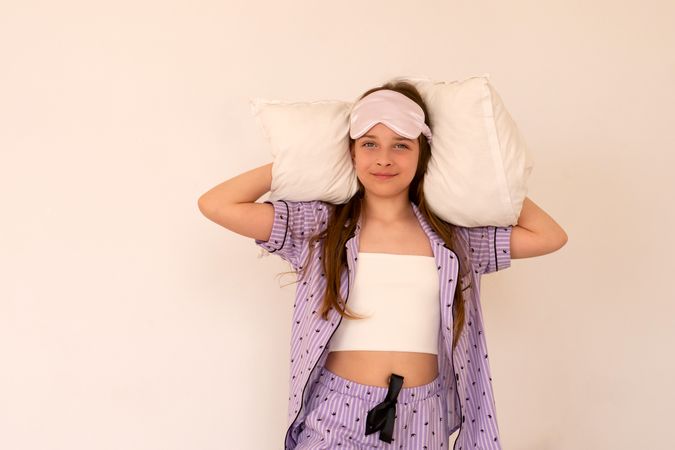 Relaxed girl with pillows, wearing sleep mask and pajamas.