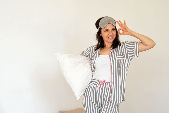 Woman making OK sign with hand, holding pillow in bed.