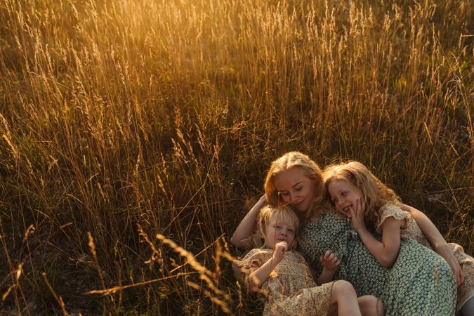 Mother hugging daughters while lying on rye field