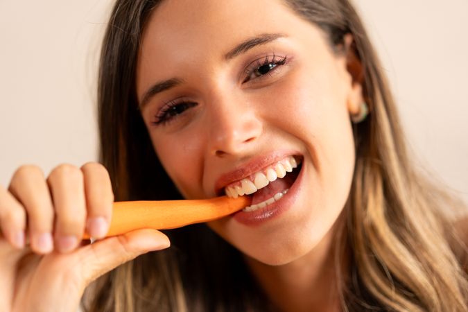 A woman is smiling and eating a carrot - healthy lifestyle habits
