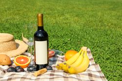 Bottle of wine, baguette, fruits, straw hat and towel on grass, space for text