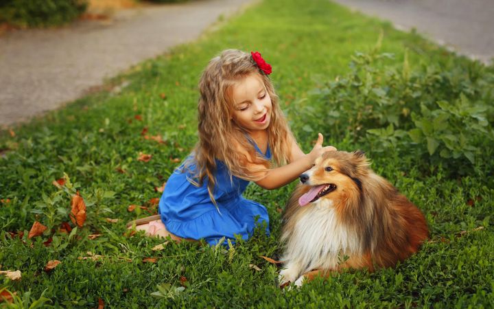 Happy female child in blue dress sitting with dog in the grass
