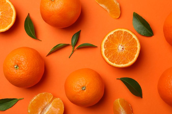 Ripe mandarins and leaves on orange background, top view