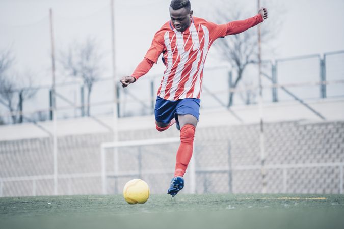 Black soccer player with red equipment playing soccer.