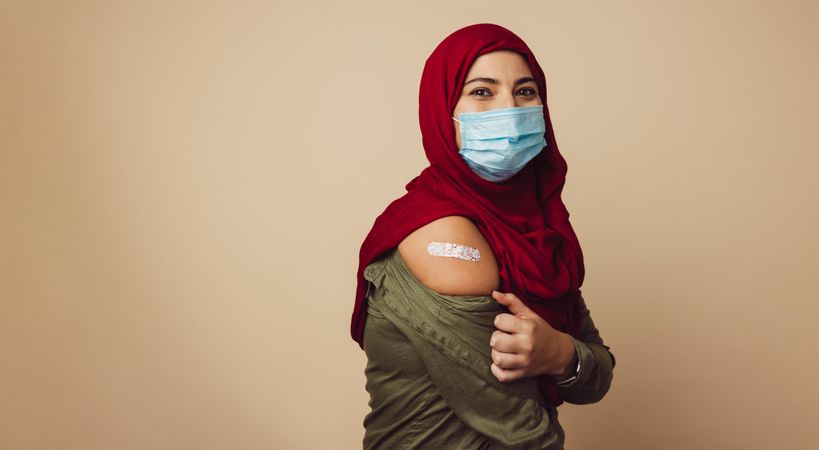 Portrait of a muslim woman showing her arm with bandage after getting vaccinated