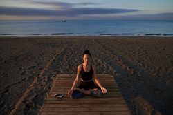 Peaceful Hispanic woman practicing lotus pose on seashore