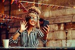 Smiling Black woman in stripe shirt waving at phone in cafe