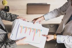 Businesswoman handing analytics document papers to another colleague