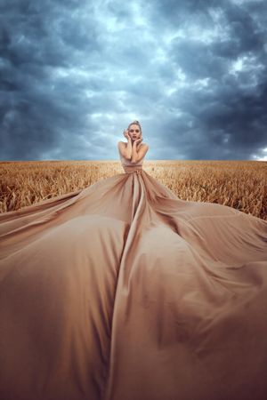 Woman in big brown dress in wheat field under cloudy sky