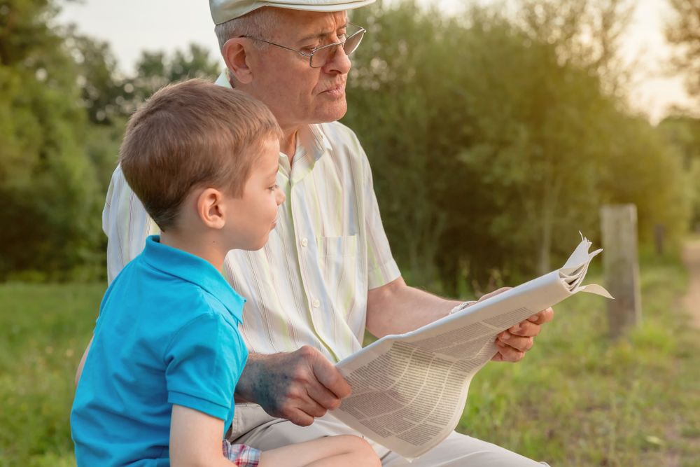 Grey haired man and child reading a newspaper outdoors