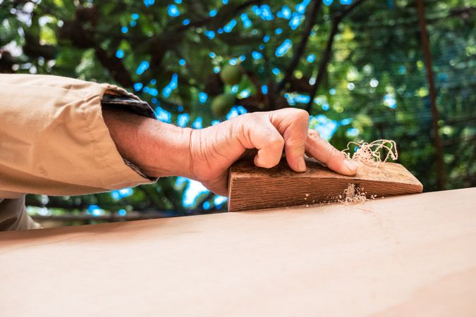 Anonymous older man shaping wood with plane tool