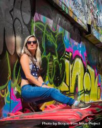 Woman in crop top and blue denim jeans leaning on graffiti wall 5aMBK5