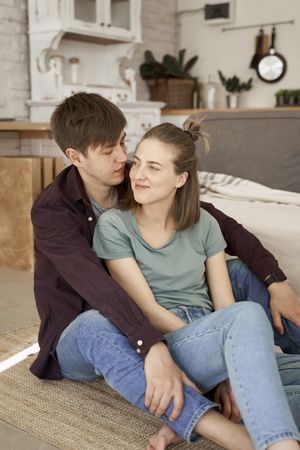 Relaxed couple hugging while sitting together on floor in living room