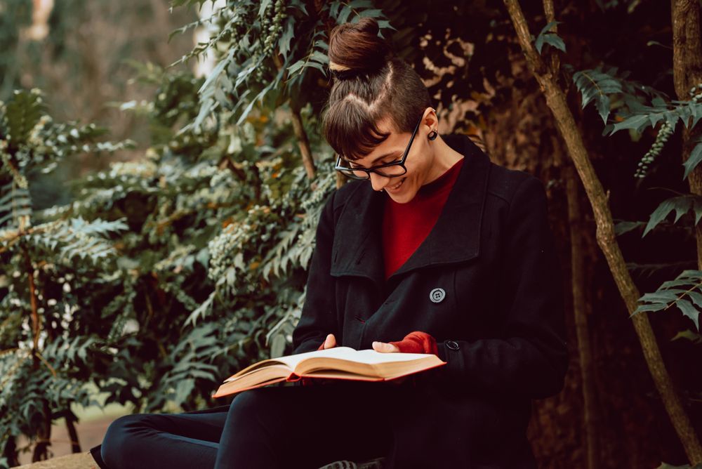 Young woman reading book on bench in park
