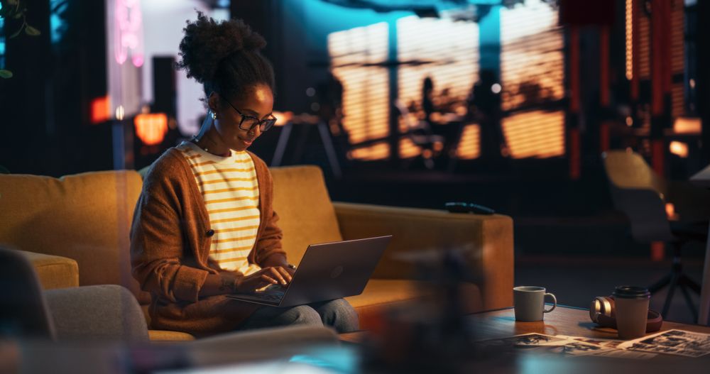 Portrait of Black Creative Young Woman Working on a Laptop in Creative Office at Night.