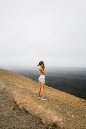 Side view of woman taking picture of sea from hill