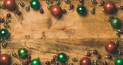 Green, red, and gold tree ornaments arranged on wooden board with copy space in center