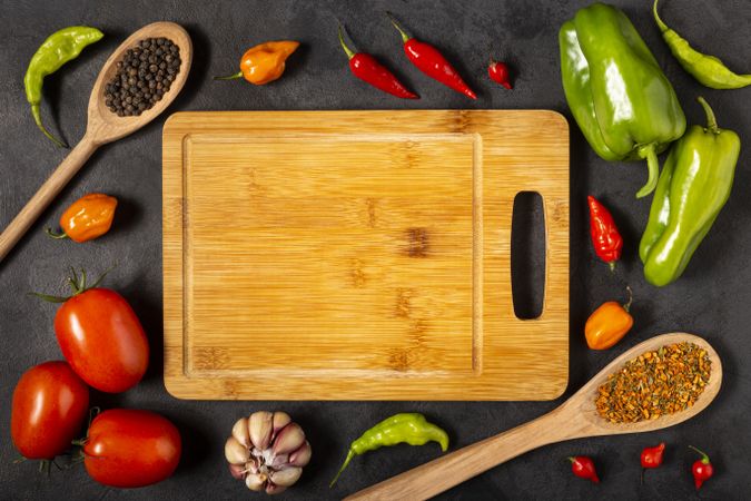 Empty cutting  board on the table with Ingredients for cooking. Tomatoes, various peppers, garlic and green peppers.