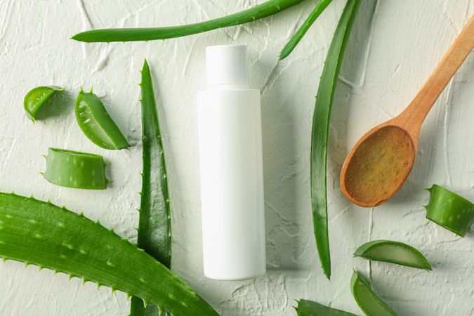 Cream bottle with space for text, wooden spoon, aloe vera slices and leaves on table, top view. Natural treatment
