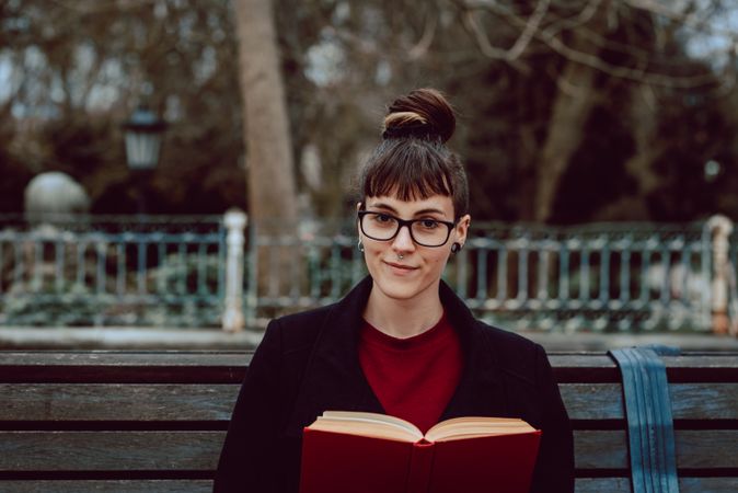 Young woman reading book on bench in park